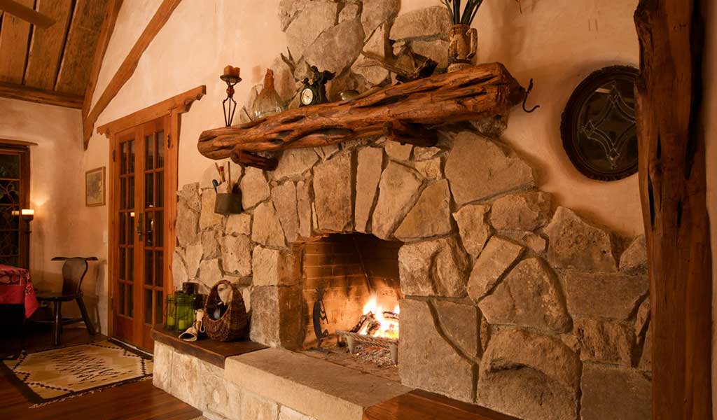 large rustic stone fireplace complemented by natural wood floors Photo: I Love Cob