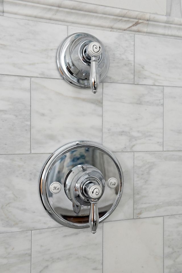 Chrome bathroom fixtures with white details on marble shower tile 
