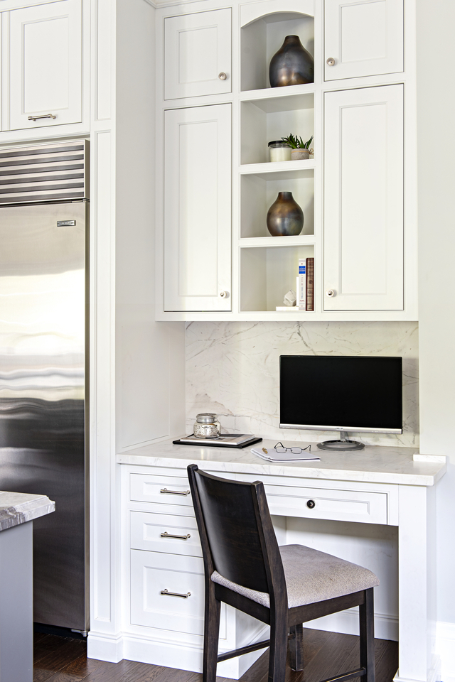 Desk nook built into corner in white kitchen with computer and chair 