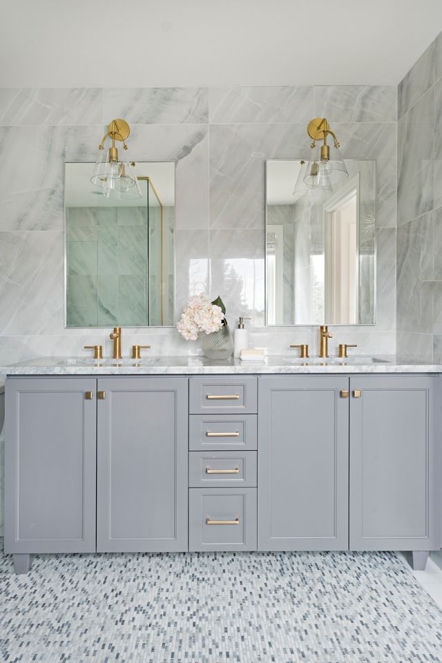 Floor to ceiling tiled bathroom with gray vanity and bronze fixtures